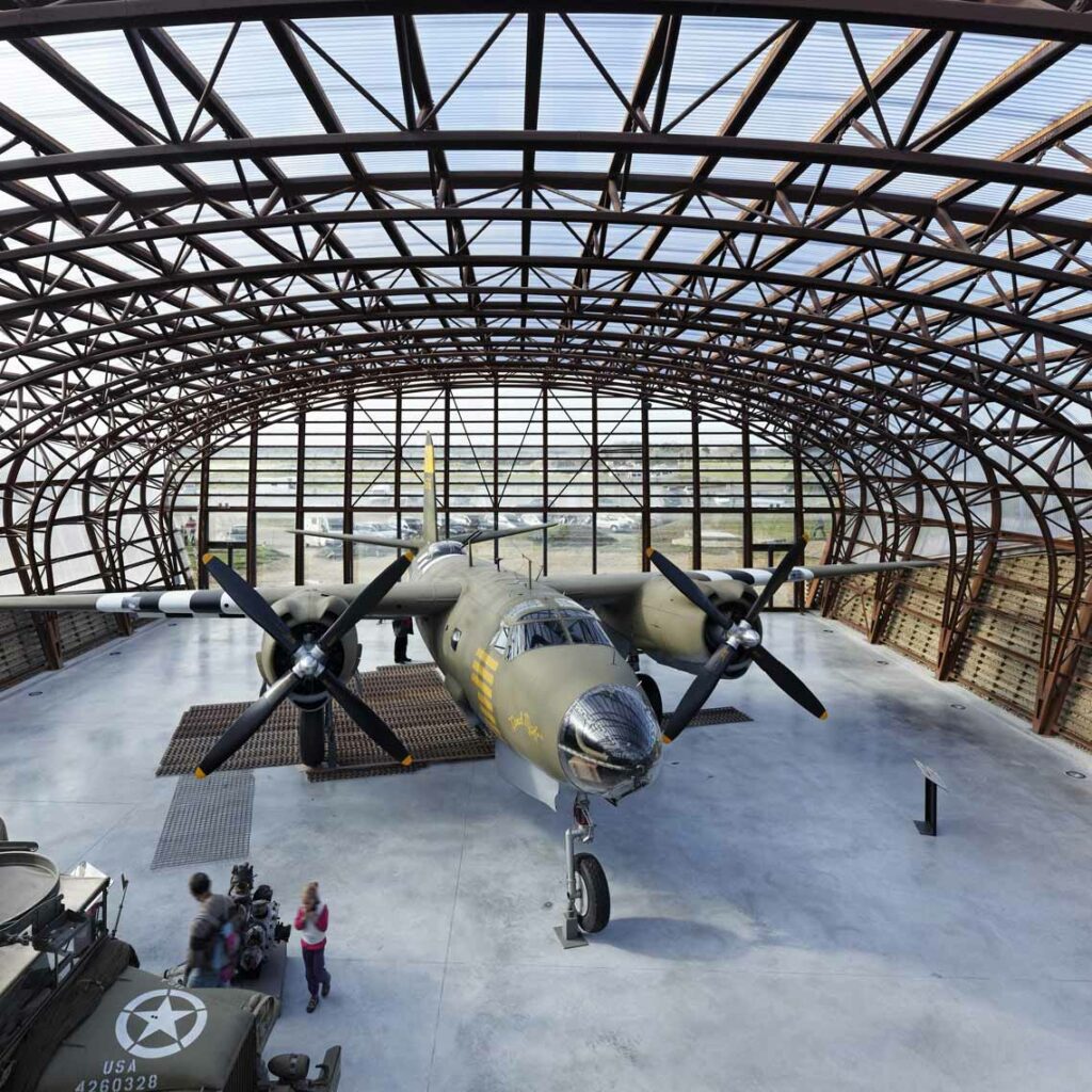 Visitors exploring vintage military aircraft at Utah Beach Landing Museum in France, showcasing World War II history and artifacts.