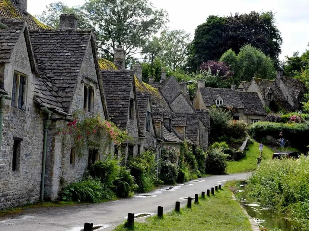 Traditional Cotswold stone cottages with climbing roses and lush greenery in a quaint English village.