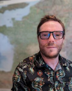 Johnny from Luxury France Tours, smiling in a patterned shirt with a map background, enhancing the team's experienced, global perspective.
