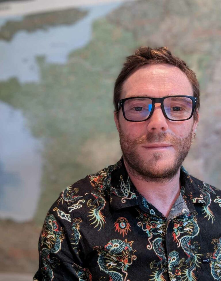 Johnny from Luxury France Tours, smiling in a patterned shirt with a map background, enhancing the team's experienced, global perspective.