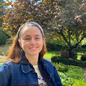 Smiling woman in a denim jacket at a lush park in France, Gabrielle France profile picture for Luxury France Tours.