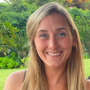 Smiling woman with a friendly face, possibly a tour guide, set against a lush garden background in France.