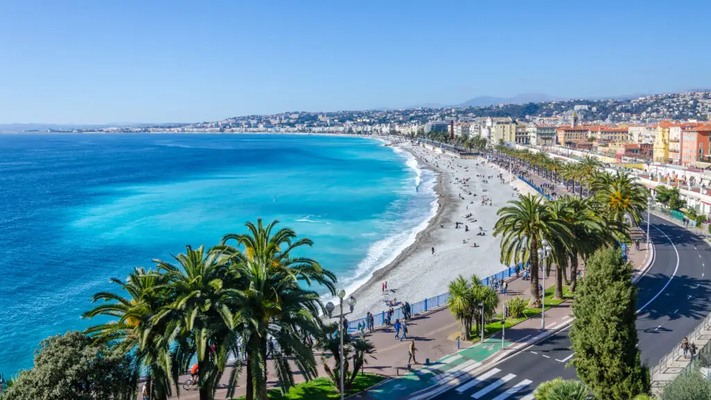 Breathtaking panoramic view of the Bay of Angels in Nice, France, showcasing the vibrant azure waters, bustling beach, and palm-lined promenade.