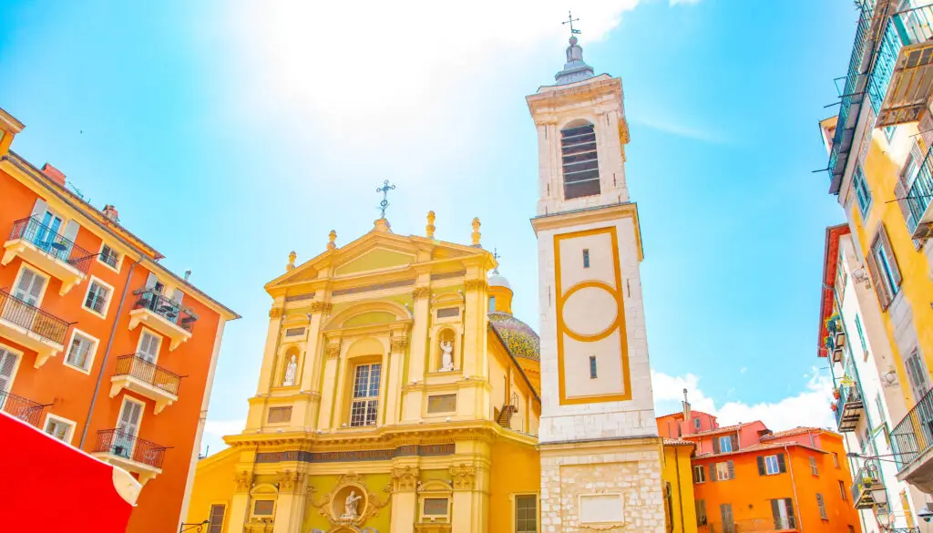Bright and colorful scenic view of Nice old town with the Cathedral standing prominently amidst vibrant buildings under a clear blue sky, France.