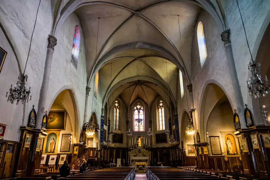 Interior view of L' Église Notre-Dame d'Espérance in Cannes, France, showing ornate Gothic architecture, stained glass windows, and historical artifacts.