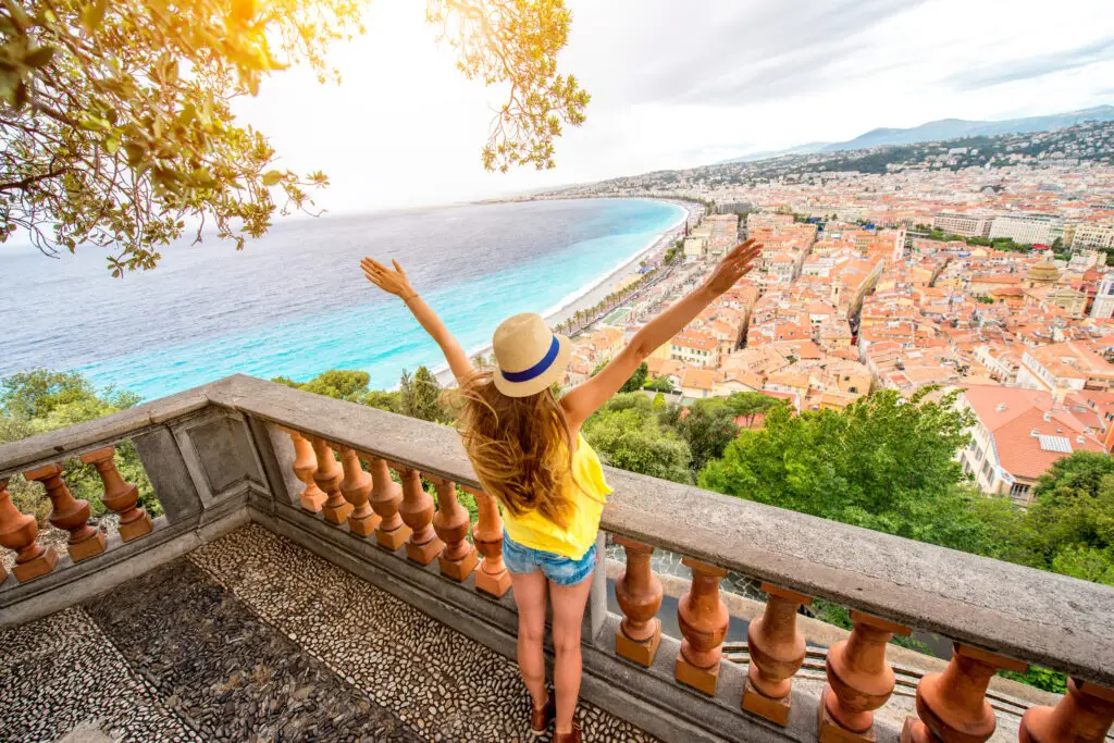 Tourist woman enjoying panoramic view of Nice, France from a high vantage point, expressing joy with arms raised.