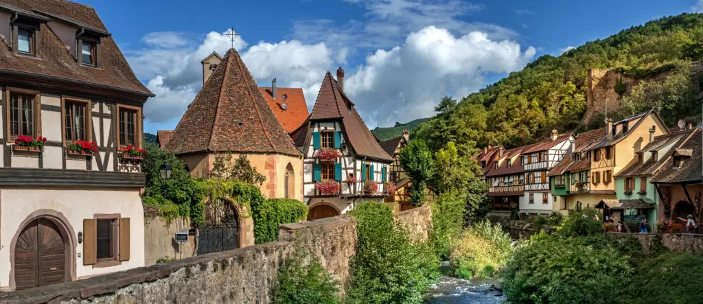 Scenic view of Kaysersberg village with traditional Alsatian half-timbered houses and lush greenery along the river in France
