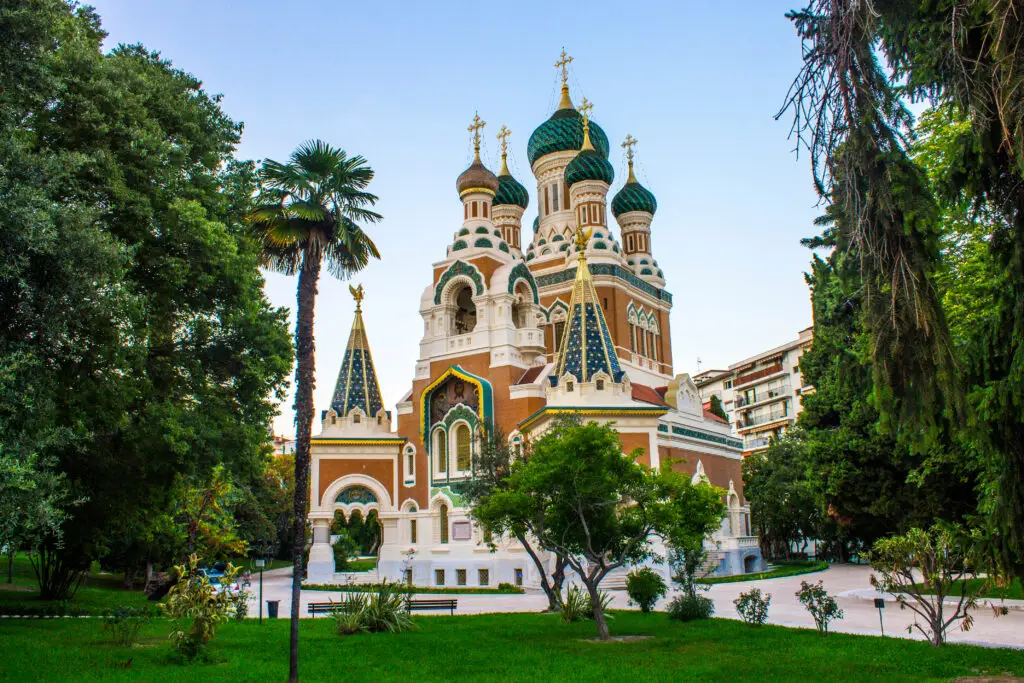 St. Nicholas Orthodox Cathedral in Nice, France, surrounded by lush green park and palm trees under clear blue sky.