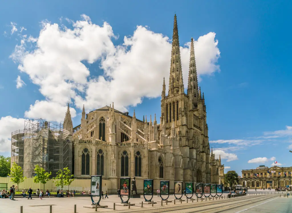 Tourist passing by the historic Cathédrale Saint-André de Bordeaux on a sunny day, showcasing the intricate Gothic architecture and ongoing restoration work.