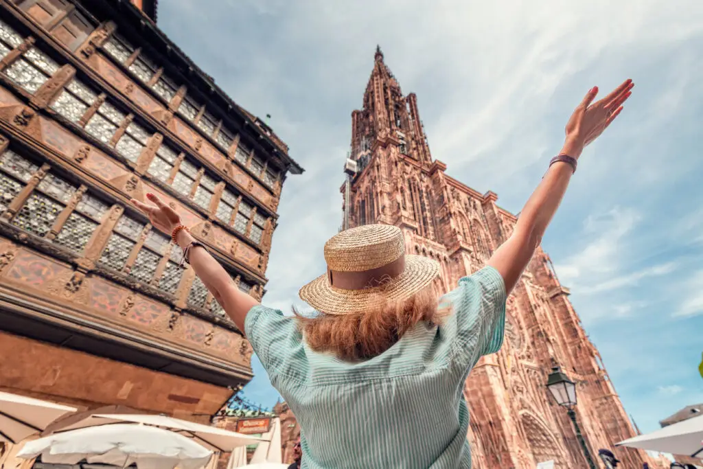 Happy tourist woman with raised arms admiring the stunning architecture of Notre Dame Cathedral in Strasbourg, France