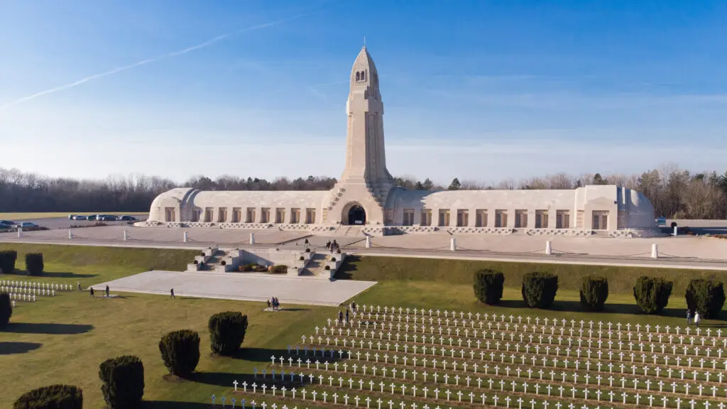 Aerial view of the Douaumont Ossuary at Verdun battlefield, a WWI memorial site in France, with rows of white crosses and visitors walking around.