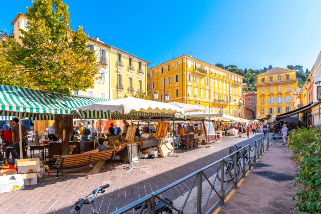 Vibrant scene at Cours Saleya Market in Vieux Nice, showcasing bustling market stalls and historic yellow buildings under a clear blue sky.