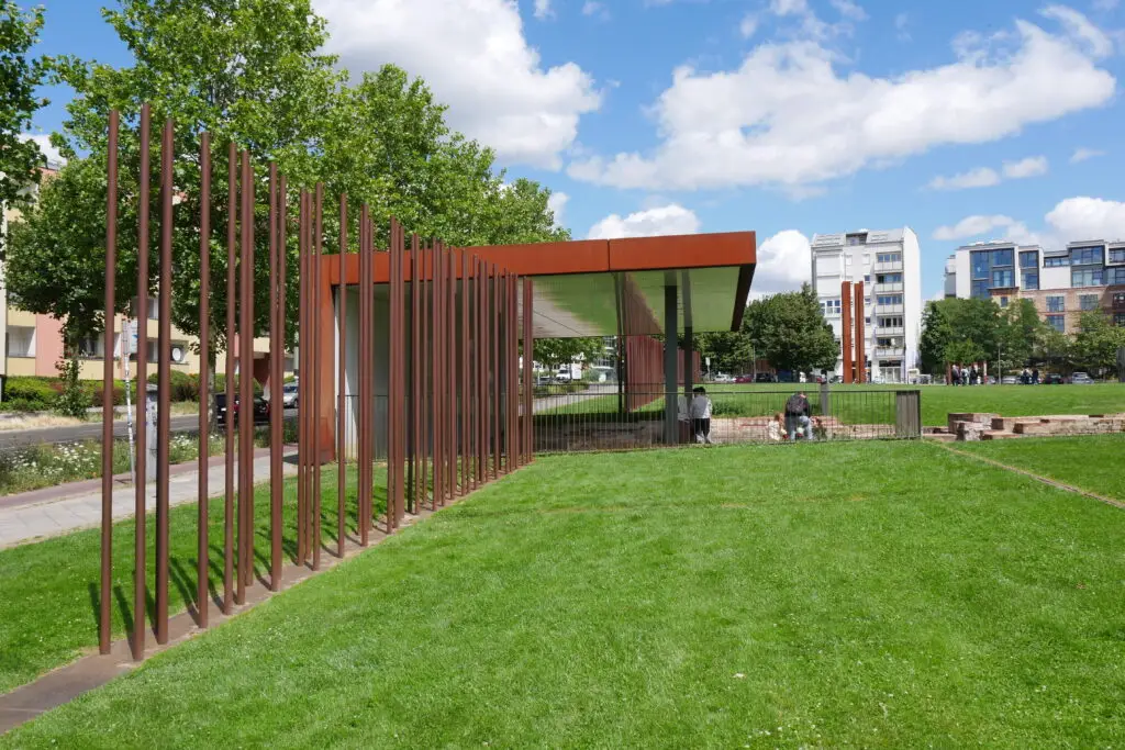 Visitors at the Berlin Wall Memorial on Bernauer Straße in Berlin, showcasing the historical remnants and modern architecture on a sunny day.
