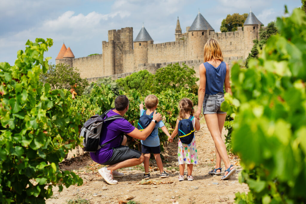 Family exploring vineyards with view of historic Carcassonne castle in France, showcasing tourist attraction with children
