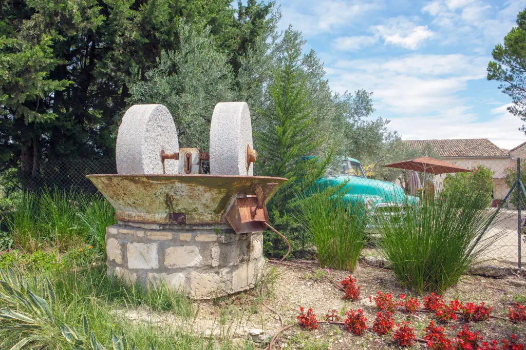 Ancient olive oil production machinery with stone mill and mechanical press set in a rural landscape in Provence, France, showcasing traditional agricultural tools amidst lush Mediterranean greenery.