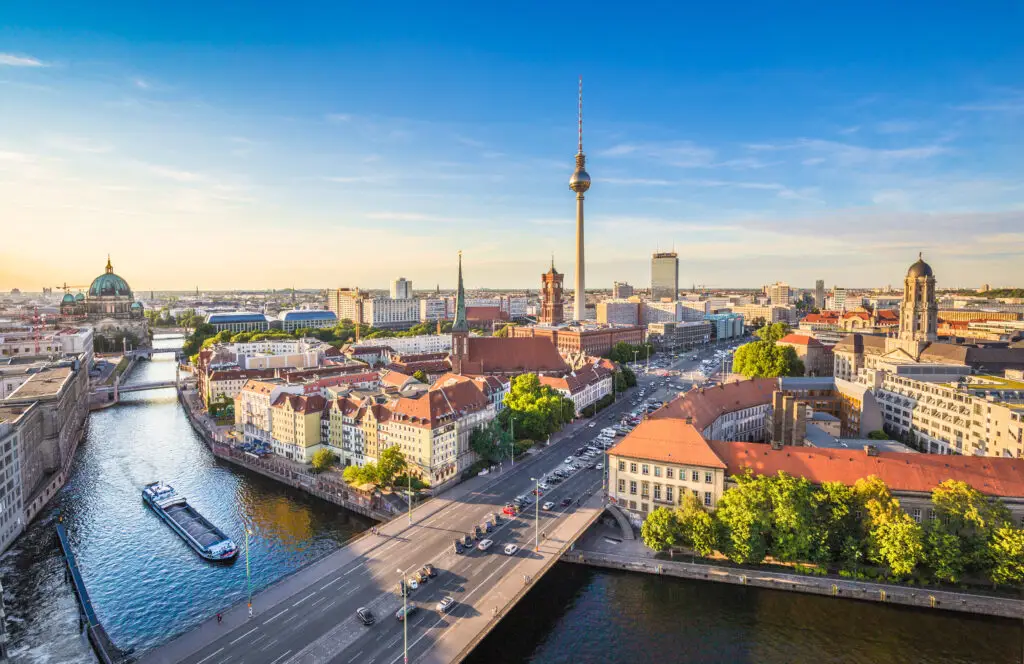 Panoramic view of Berlin skyline at sunset featuring the iconic TV Tower and Spree River with a boat cruising