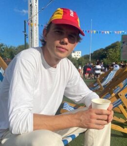 Luke, a young male tour guide from Luxury France Tours, seated outdoors with a coffee in a relaxed setting, promoting friendly and personalized guided tours in France.