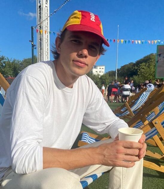 Luke, a young male tour guide from Luxury France Tours, seated outdoors with a coffee in a relaxed setting, promoting friendly and personalized guided tours in France.