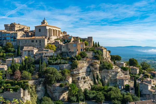Panoramic view of Gordes, a picturesque hilltop town in Provence, France, showcasing historic stone buildings and lush greenery under a clear blue sky.