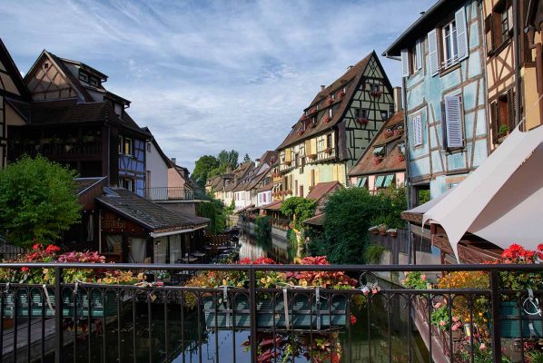 View from an ornate bridge looking over a river lined with Wooden framed 13th century buildings in Colmar, France